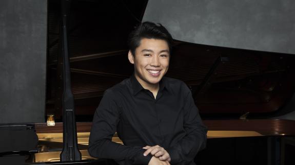 Der Pianist George Li lächelt und sitz vor dem Klavier