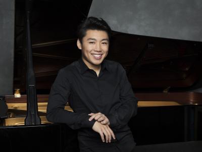 Der Pianist George Li lächelt und sitz vor dem Klavier